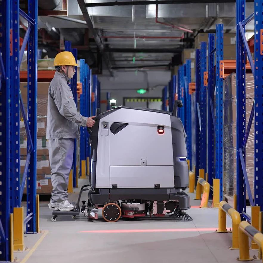 PUDU BG1 scrubber-dryer working in a warehouse aisle between racks